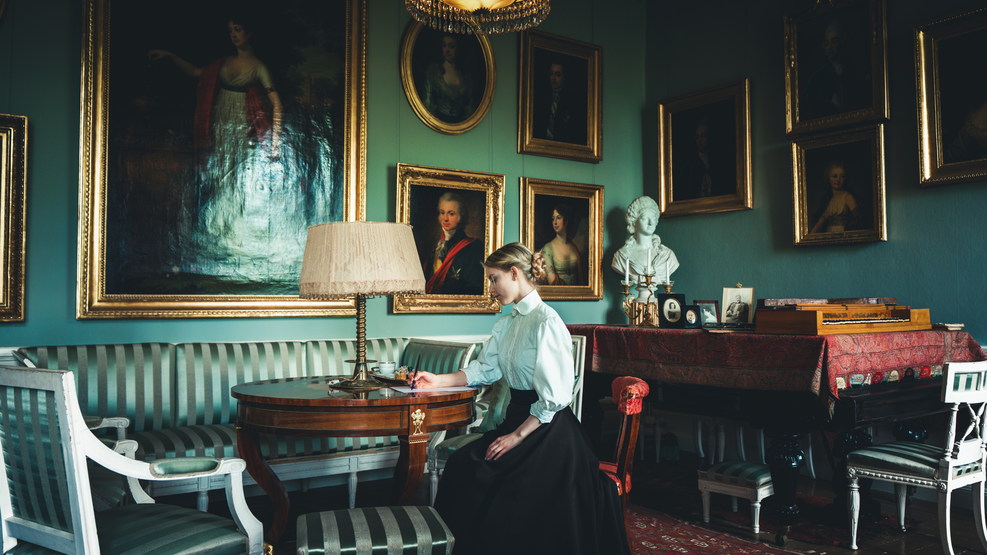 Statist i tidstypiska kläder sitter ner och skriver ett brev på Löfstad slott.